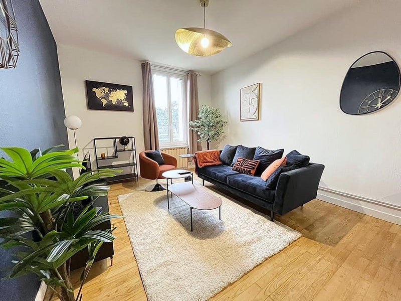 Séjour meublé : canapé velours bleu nuit, fauteuil terracotta, tapis blanc, suspension dorée
