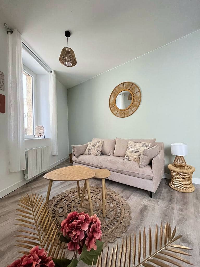 Séjour meublé : canapé rose poudré, tables gigognes bois, miroir en rotin, tapis en jute